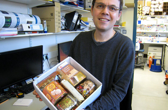 Christian Speck displays a box of German Christmas treats, a gift from of lab alumnus, Stefan Samel